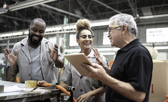 At a workbench, in a factory, colleagues smiling